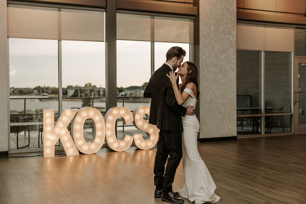 A romantic first dance between newlyweds under elegant lighting in a modern reception venue with KOCO signage.