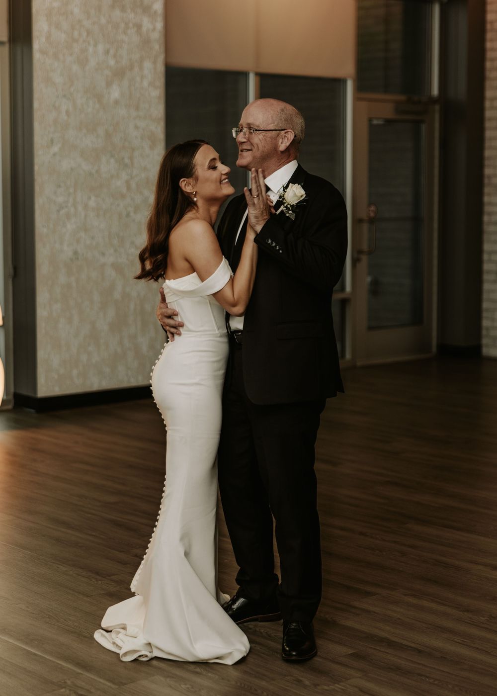 A tender father-daughter dance moment at a wedding reception shows an emotional embrace on a wooden dance floor.