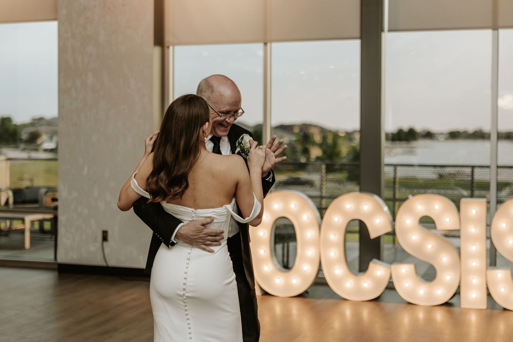 A romantic first dance moment against illuminated marquee letters at an indoor wedding reception.