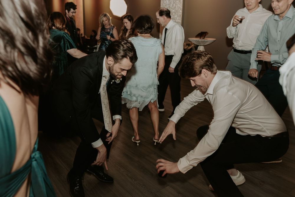 Wedding guests dancing energetically on wooden dance floor during reception party.