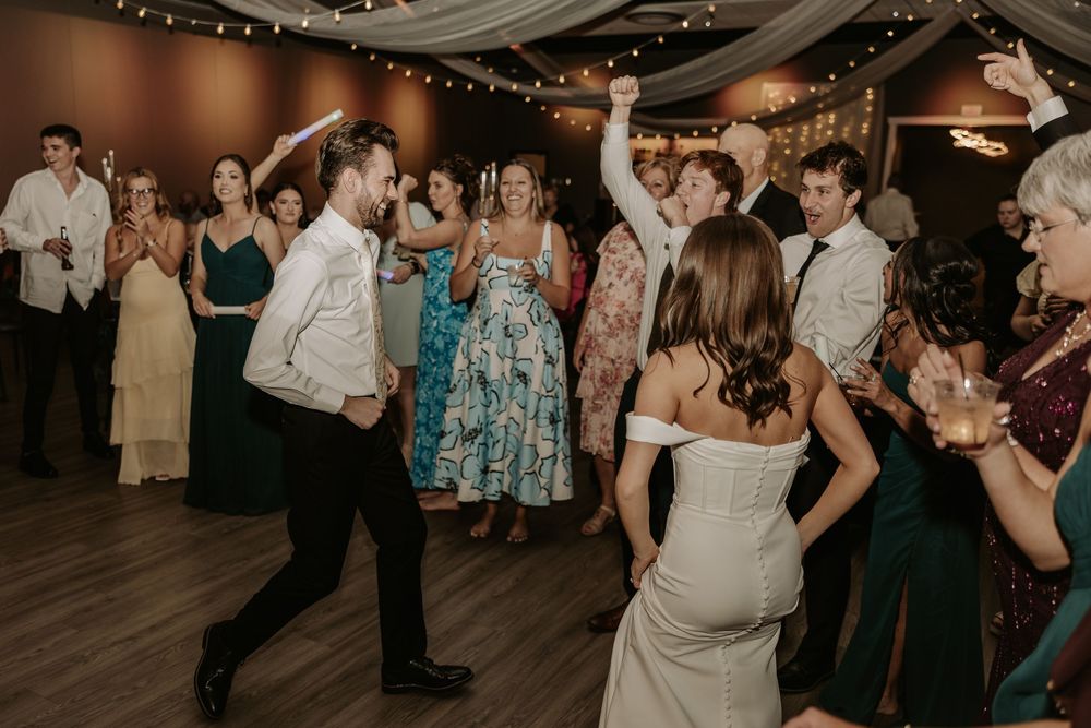 Wedding guests dancing and celebrating at an indoor reception with dim lighting and festive atmosphere.