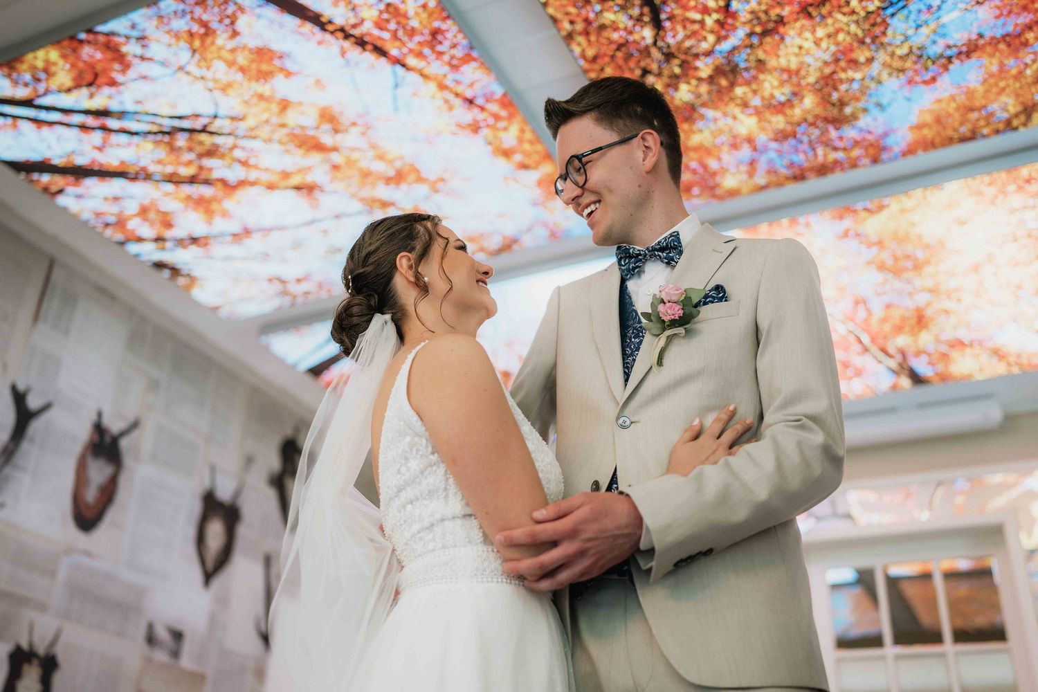 Wedding couple shares intimate moment under ceiling painted with autumn leaves.