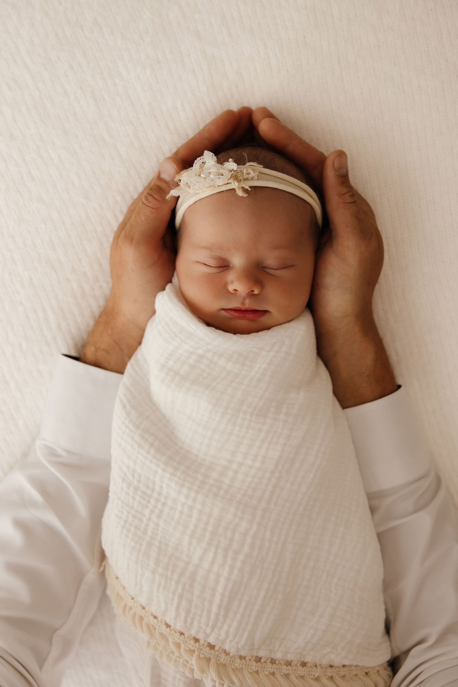 A sleeping newborn baby swaddled in cream-colored fabric lies peacefully in multiple similar poses.