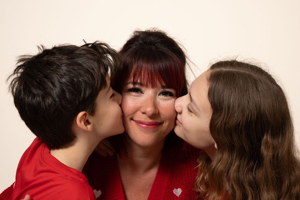 Famille en vêtements rouges partageant de doux baisers et des sourires dans un portrait en studio.