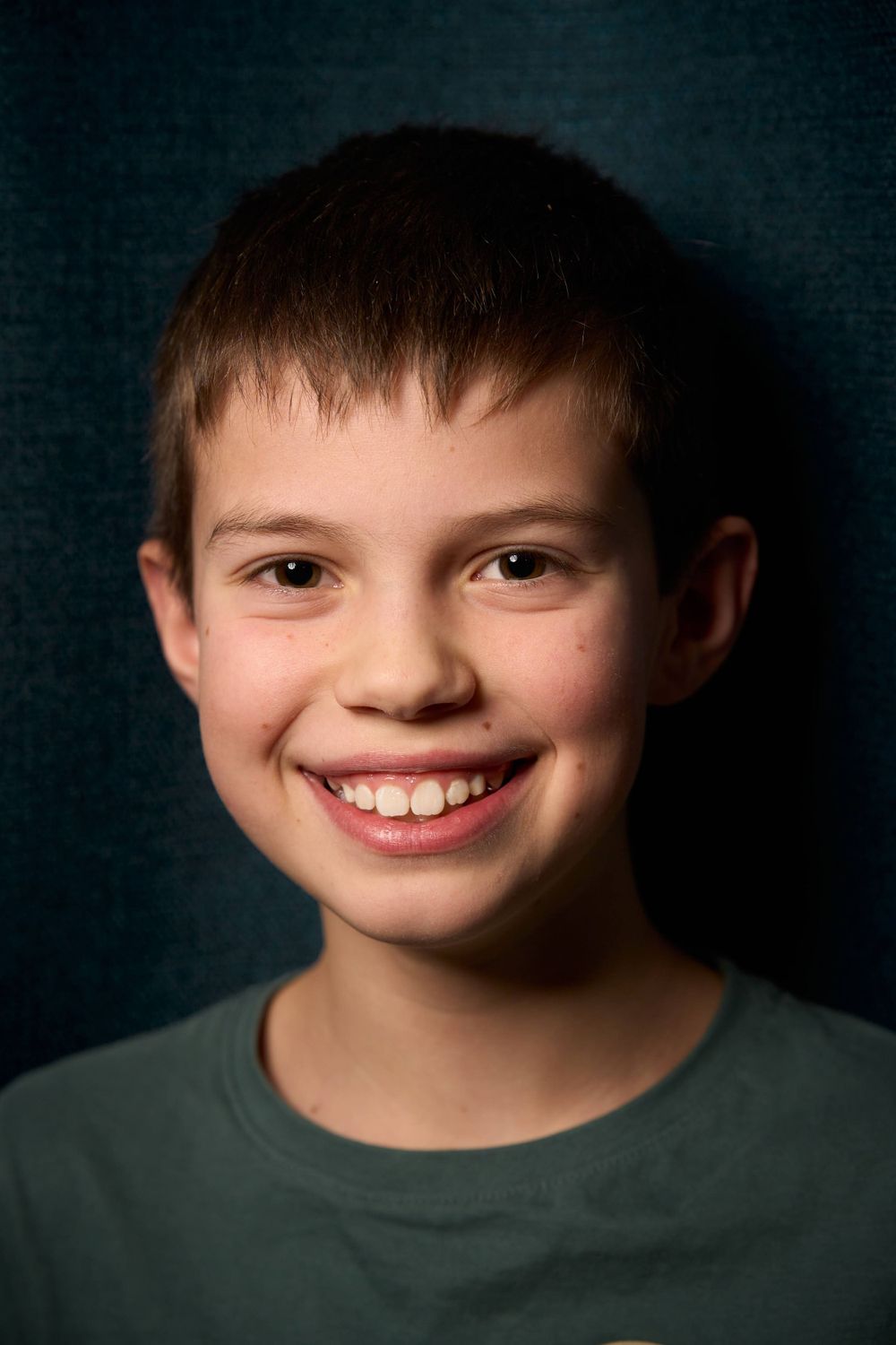 Portrait d'un jeune garçon en chemise verte sur fond sombre.