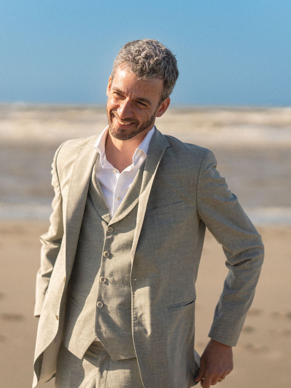Portrait décontracté en costume beige souriant sur une plage de sable.