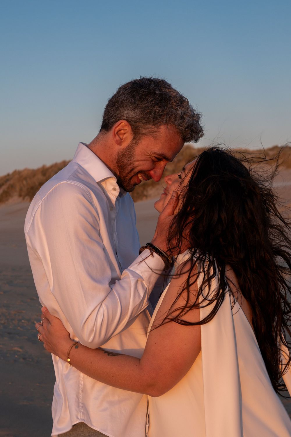 Un couple romantique en vêtements blancs partage un moment intime au coucher du soleil sur une plage.