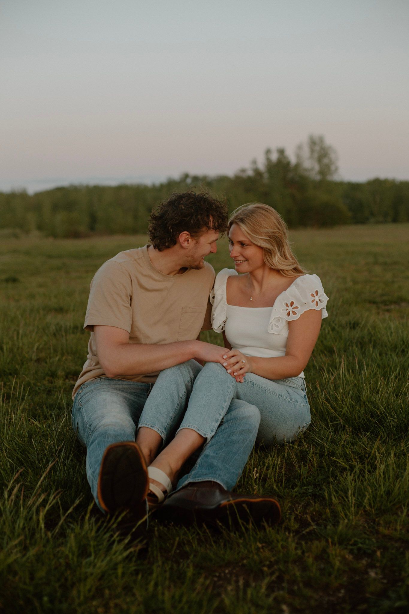 Couple sitting in a field looking at each other with legs overlapping during Grand Rapids engagement session.