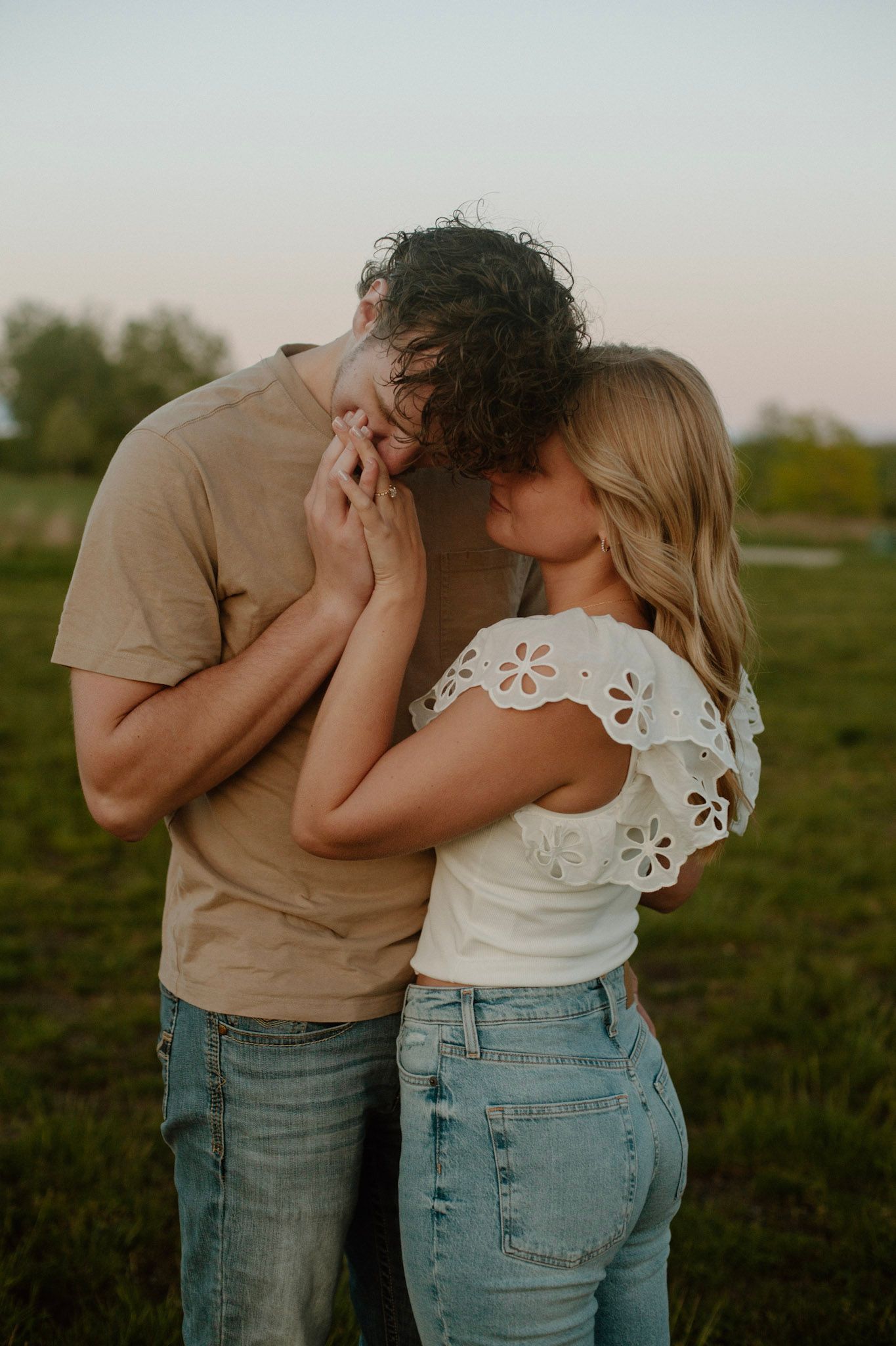 Couple embracing during their engagement session at Millennium Park in Grand Rapids MI and he is kissing her hand.