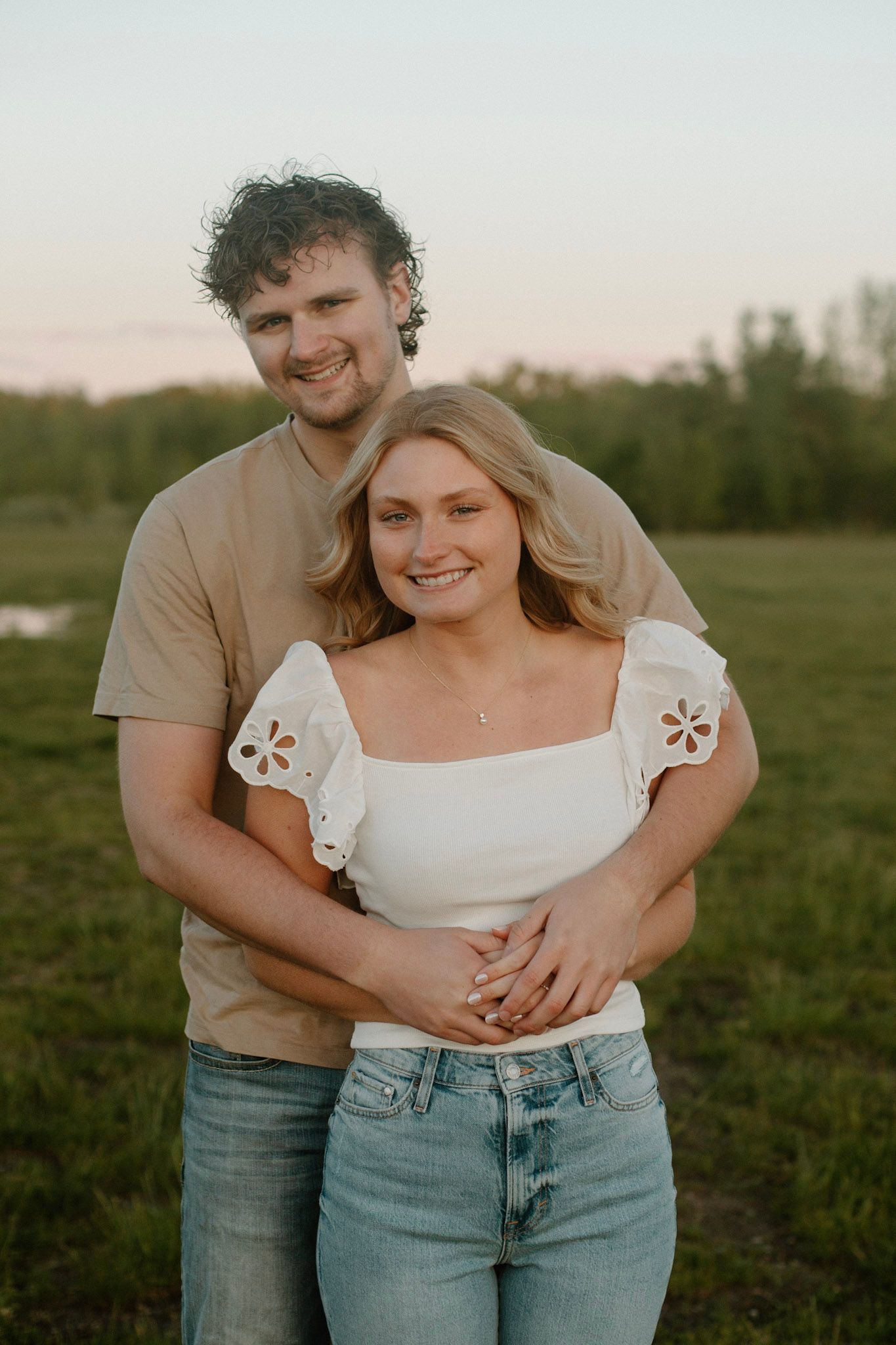 Couple with his arms wrapped around her from behind during engagement session at golden hour.