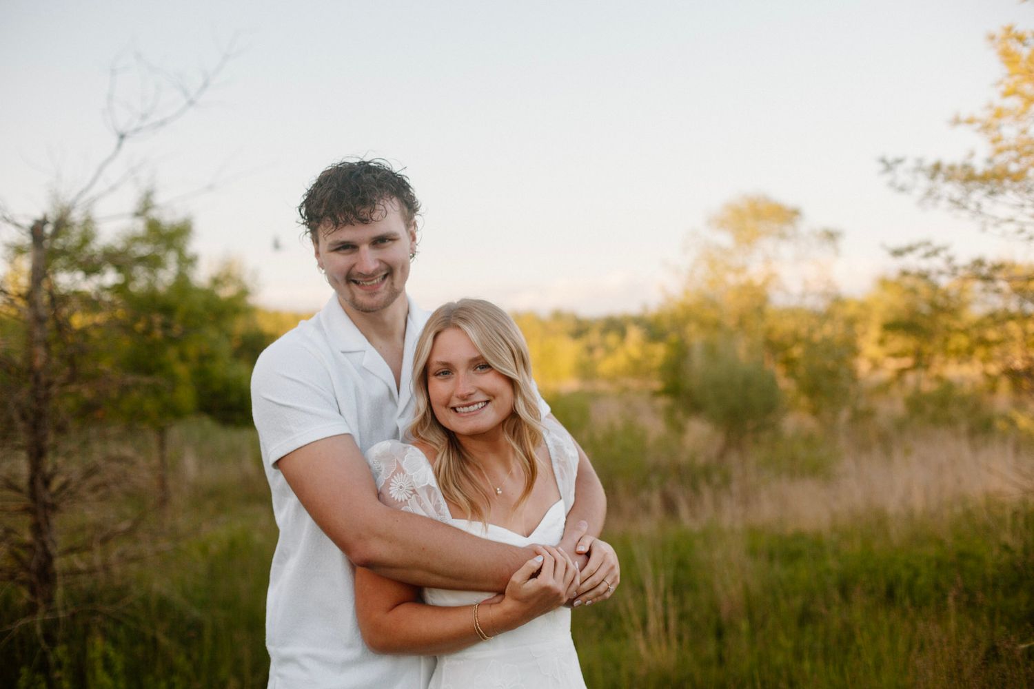 Couple with his arms wrapped around her from behind during engagement session at golden hour.