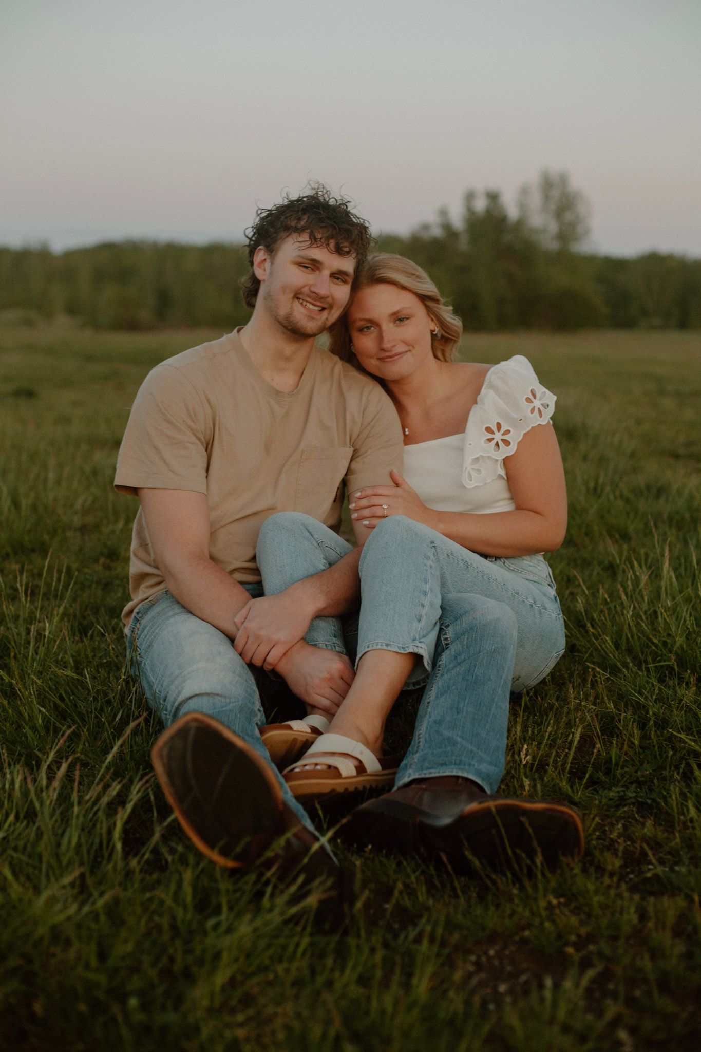 Couple sitting in a field looking at the camera with legs overlapping during Grand Rapids engagement session.