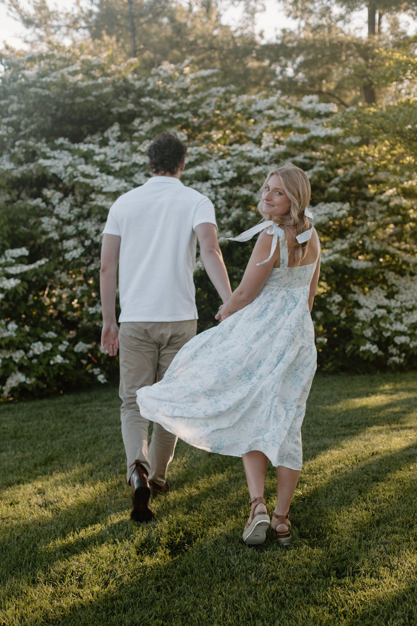 Couple walking away and she is looking back over her shoulder smiling during their engagement session at Millennium Park in Grand Rapids MI.
