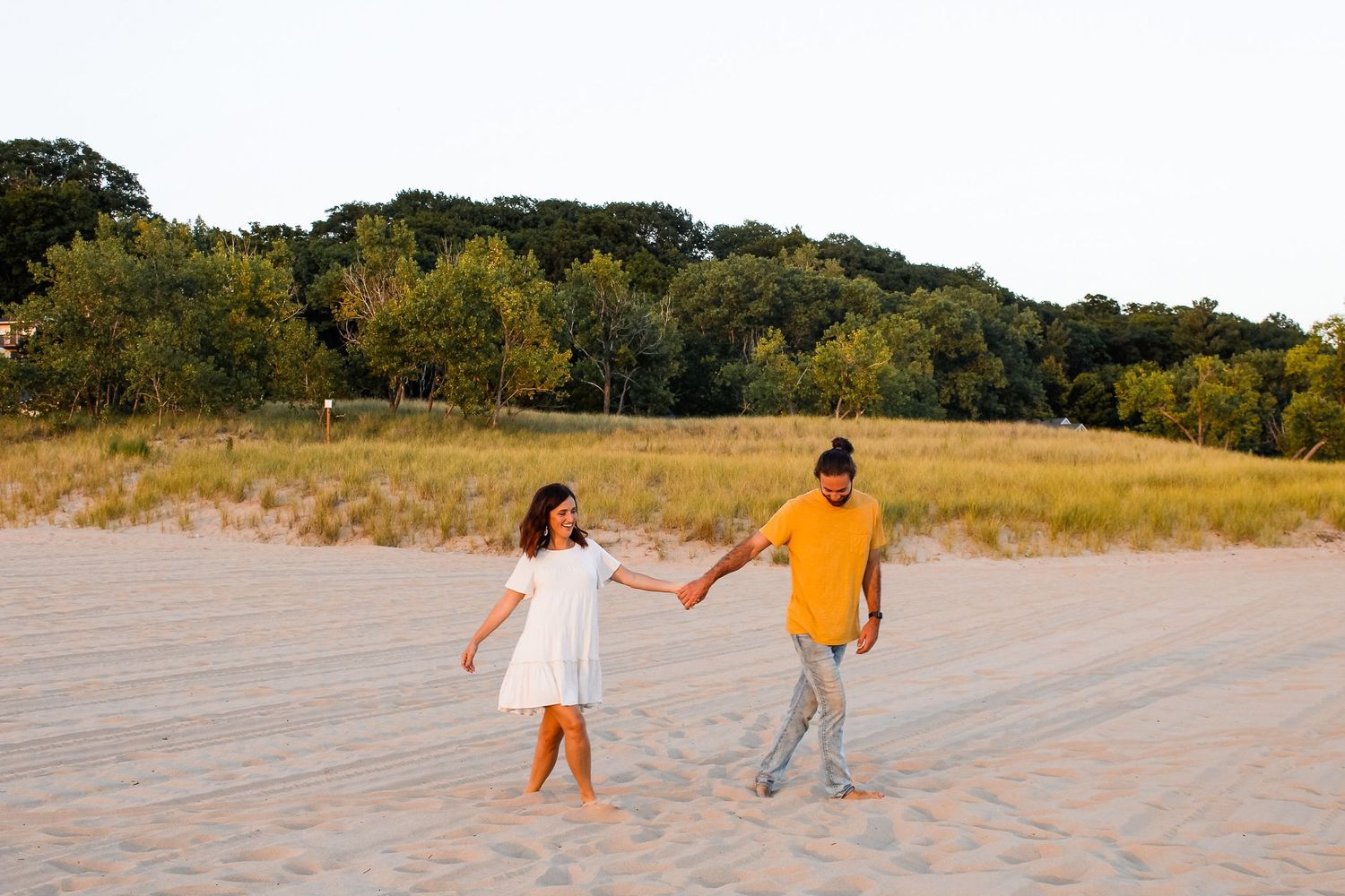 Couple walking through the sand at Holland State Park during their engagement session.