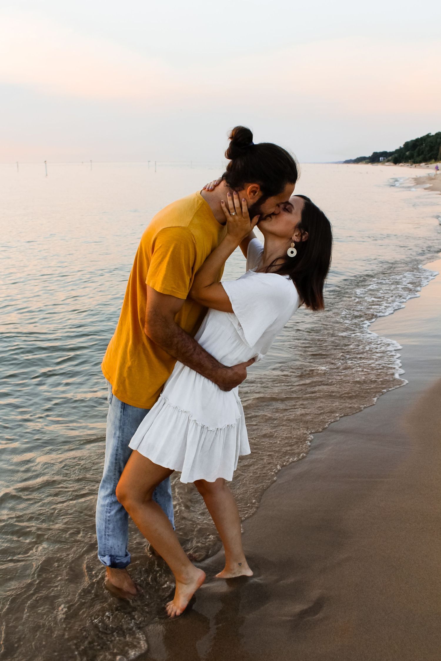 Couple embracing in front of Lake Michigan during their engagement session in Holland, MI.