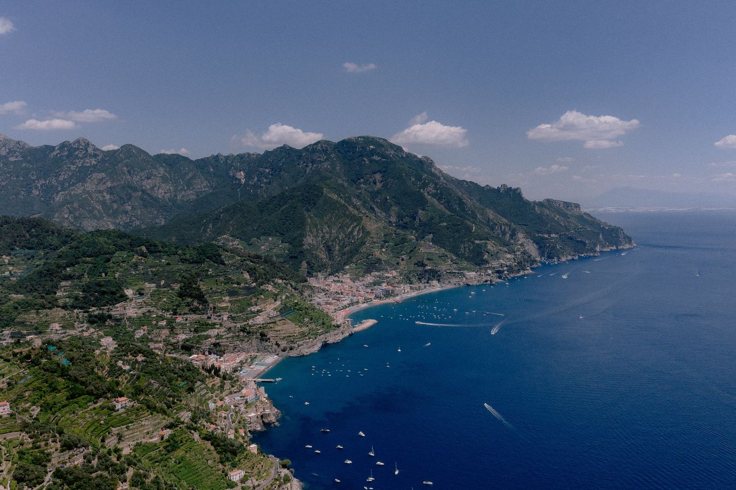 Aerial view of the Amalfi Coast in Italy showing dramatic cliffs, turquoise waters, and scattered boats along the coastline.