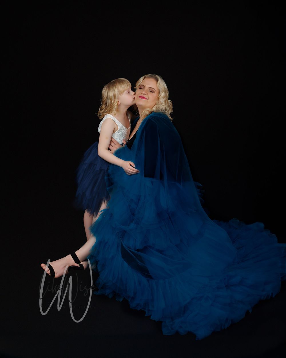 A heartwarming portrait showing two figures in matching navy blue tulle dresses against a dark backdrop.