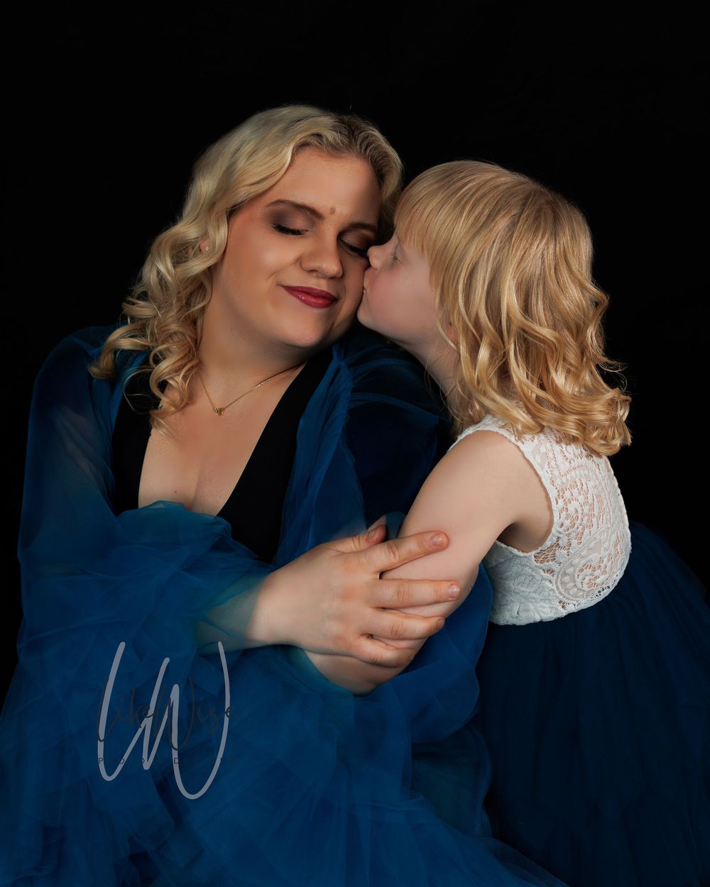 Intimate portrait showing tender moment between two people in navy blue and white against black background.