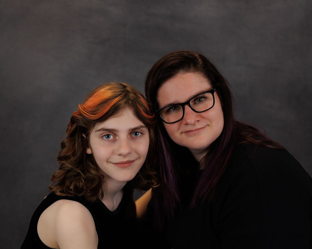 Studio portrait of two young people with curly hair against a dark gray background.