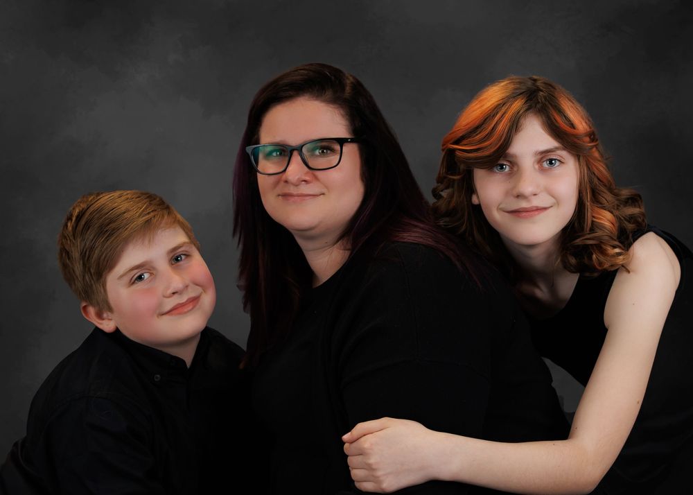 Studio portrait of three people wearing black against a dark background with dramatic lighting.