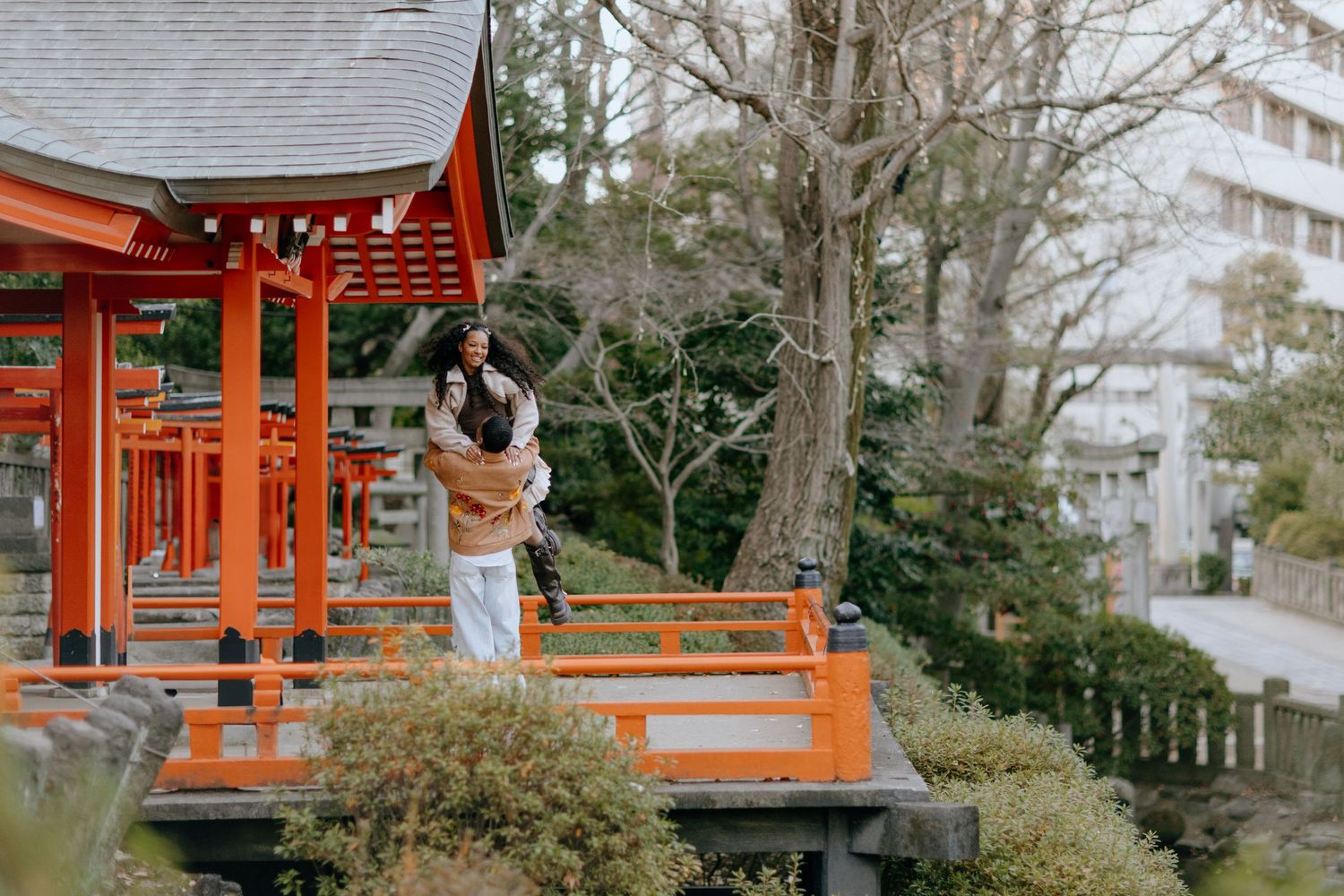Traditional Japanese garden with a red torii gate and pagoda-style structure surrounded by lush greenery in winter.