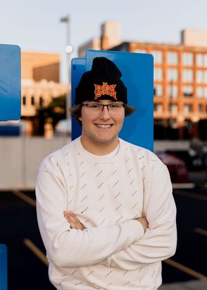 Person in white sweater and black hat poses against brick building at sunset.
