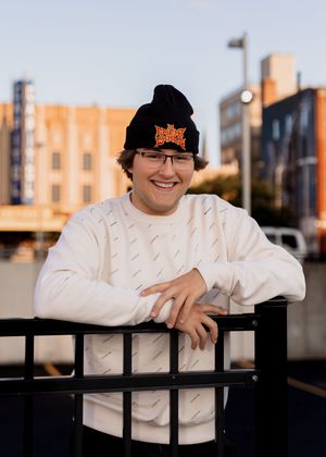 Person leaning on black railing wearing white sweater and baseball cap.