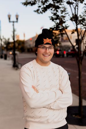 Person in white sweater and black hat poses outdoors at dusk.