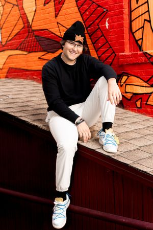 Person in black and white outfit sits against vibrant orange graffiti wall.