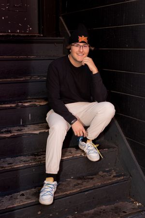 Person in casual wear sits on dark wooden steps wearing blue sneakers.