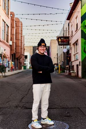 Person poses on city street with string lights and buildings in background.