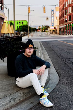 Person in casual attire sits on curb of downtown street.