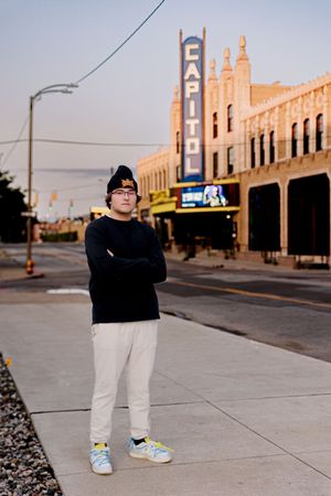 Person in black top and light pants standing on sidewalk near vintage building facade.