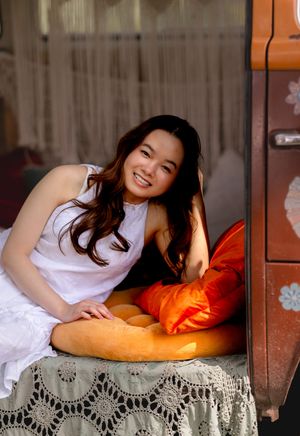 An orange pillow and lace decor create a cozy indoor portrait setting.