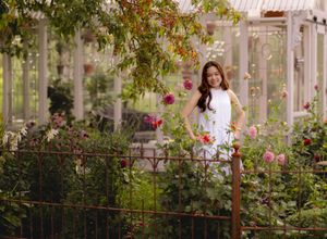 White dress portrait in a garden pergola surrounded by pink and red flowers.