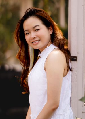 Portrait against white column wearing sleeveless white dress with ruffled neckline.