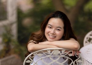 Relaxed portrait leaning on ornate white garden furniture outdoors.