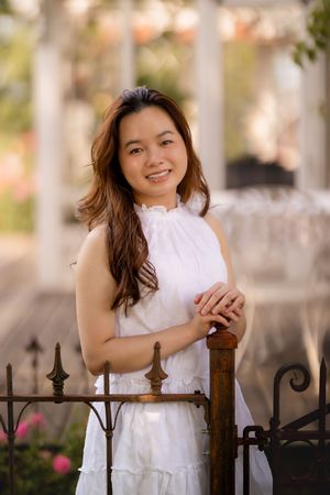 Portrait by vintage iron gate wearing white dress in garden setting.