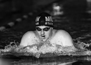 Swimmer performs butterfly stroke in black and white action shot.