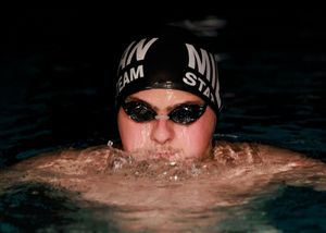 A swimmer emerges from dark water wearing a swim cap and goggles during training.