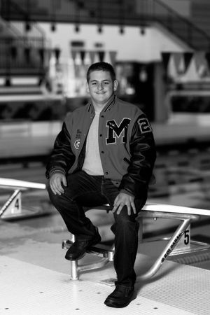 Person in varsity jacket poses on diving platform at indoor swimming pool.
