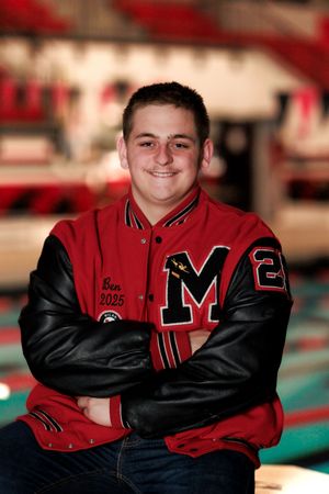 Student athlete poses in red and black varsity letter jacket by swimming pool.