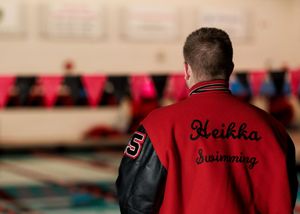Back view of Heikka Swimming varsity jacket at pool with red pennants visible.