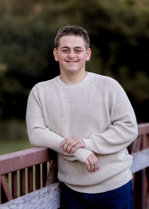 Casual portrait leaning on wooden railing wearing cream sweater outdoors.