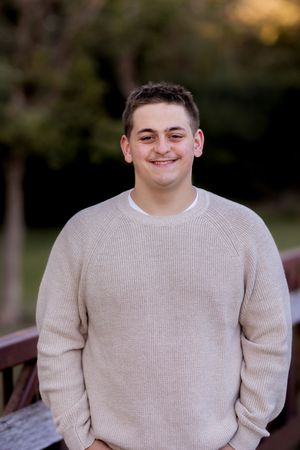 A person wearing a cream-colored sweater smiles while sitting outdoors in natural lighting.