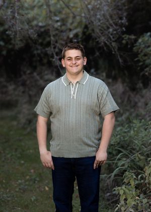 Someone in a gray short-sleeve shirt and dark pants stands outdoors in a garden setting.