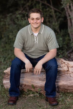 A person in casual wear sits on a fallen log during an outdoor photo session.