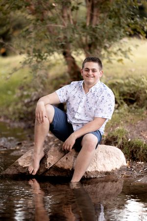 Person in summer attire sits on a rocky stream bank dangling feet in the flowing water.