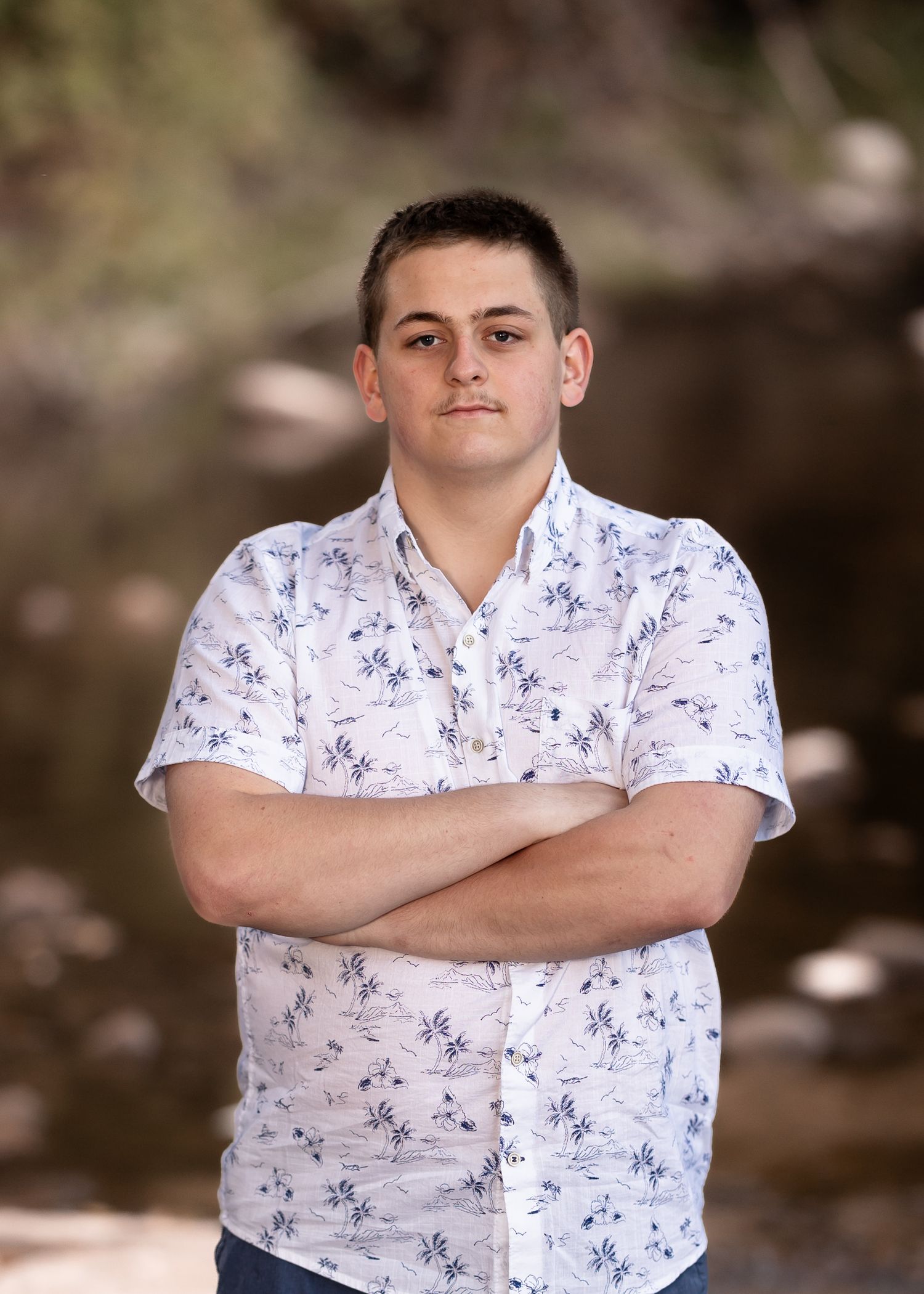 Someone poses outdoors wearing a white floral button-up shirt with crossed arms.