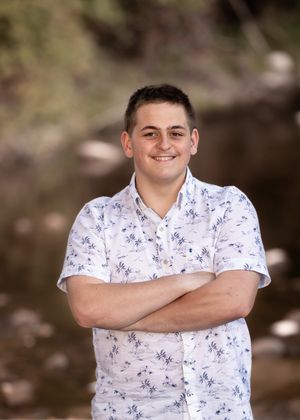 Person in white patterned shirt poses confidently against natural outdoor background.